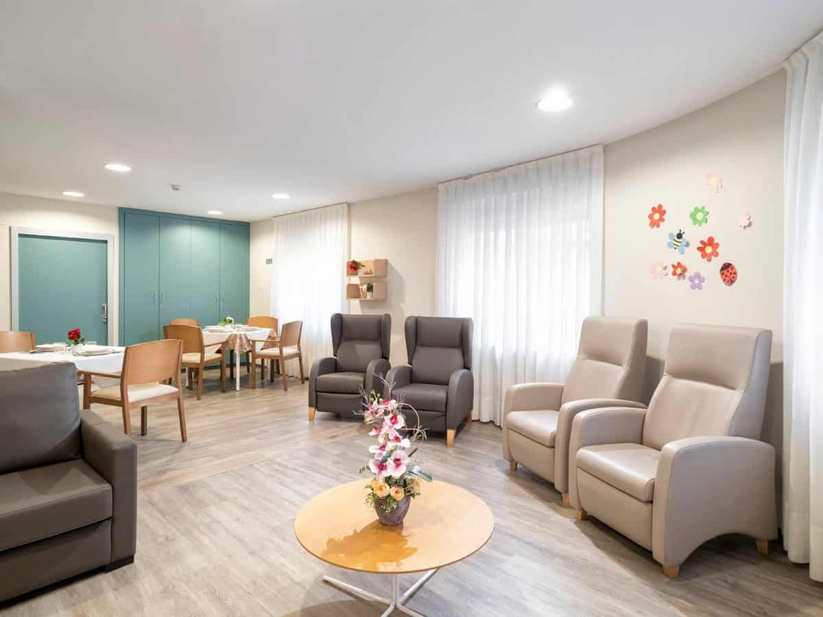 Sala de estar con sillones reclinables, una mesa de centro y un comedor con mesas y sillas de madera.