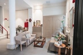 Sala de espera o recepción con sofás, un sillón, un cuadro religioso y plantas decorativas.