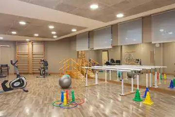 Sala de gimnasio con equipamiento de fisioterapia y ejercicio, con espejos en la pared.